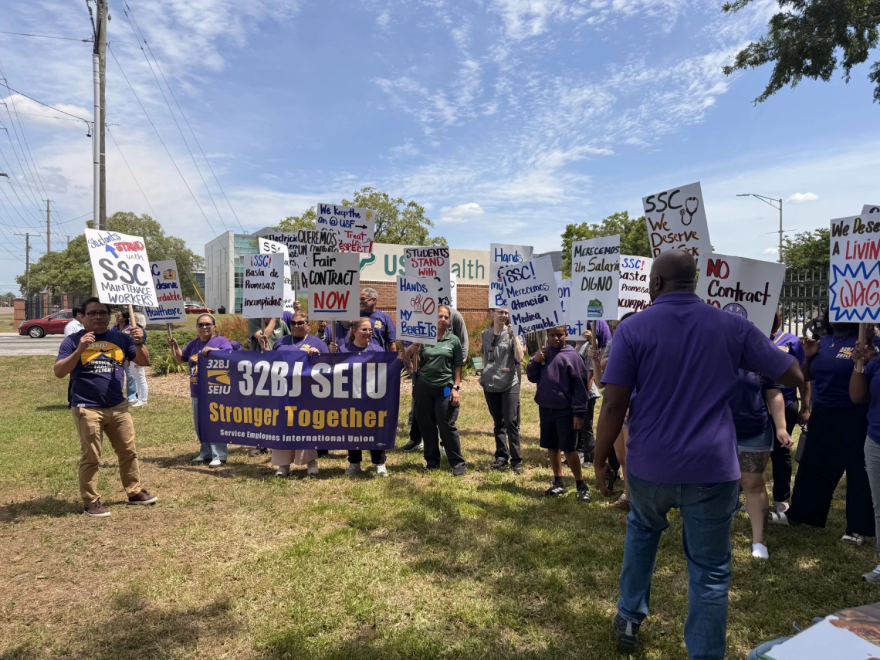 Un grupo de manifestantes, vistiendo camisetas moradas y sosteniendo carteles tanto en inglés como en español, pidiendo salarios más justos.