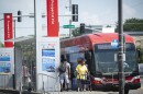 Exterior photo of a red transit bus stopped at a bus stop labeled "Prospect at 31st." People can be seen getting off the bus while others are waiting to get on.