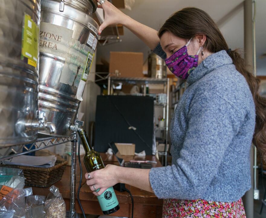 Wellspent Market’s Hannah Cable tips a drum of olive oil to fill a bottle at the Portland shop, Oct. 8, 2021. The store’s once yearly olive oil delivery from Italy has been stuck in transit for months.