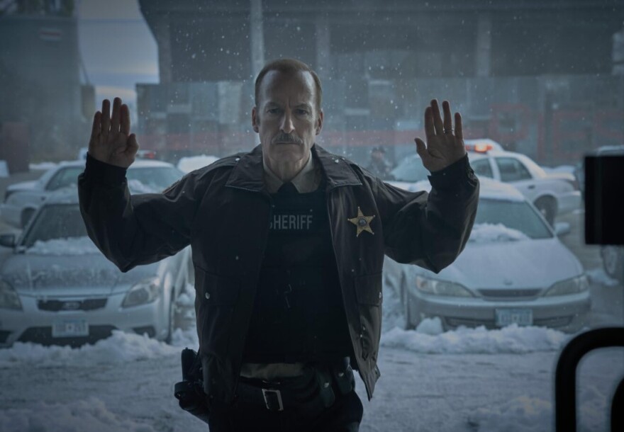 A sheriff holds up his hands as if he's being held hostage