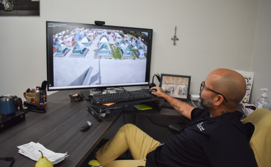 A man sitting at his desk looks at live camera footage of rows of tents outside at the Tampa Hope homeless shelter. 