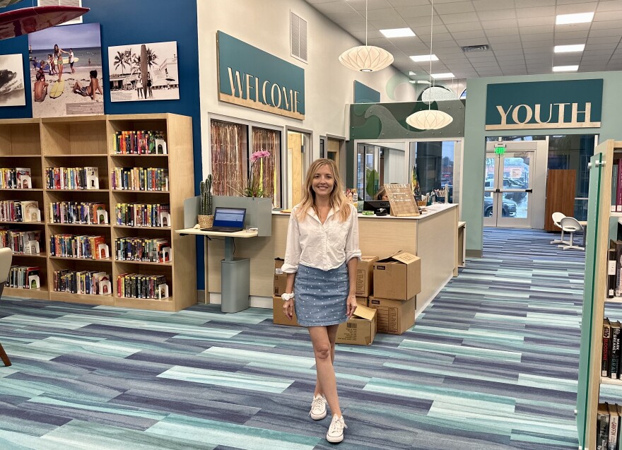 Kristine Kreidler is the director of the Lantana Public Library in the Town of Lantana. She standing near the entrance, next to a surfing exhibit.