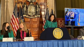 Hochul speaking behind podium next to people wearing face masks