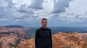 A man wearing all black stands in front of a large canyon