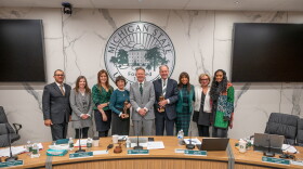 The MSU Board of Trustees and President Kevin Guskiewicz, smiling and posing for a photo together. Trustees Dan Kelly and Dianne Byrum hold small Spartan statues.