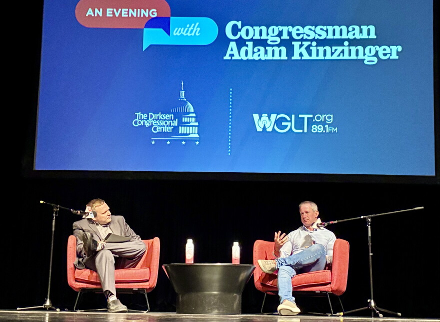 Two men chat on stage in two red chairs
