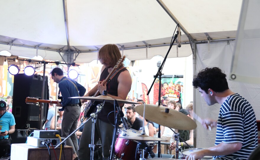 Three people perform on stage together with instruments.