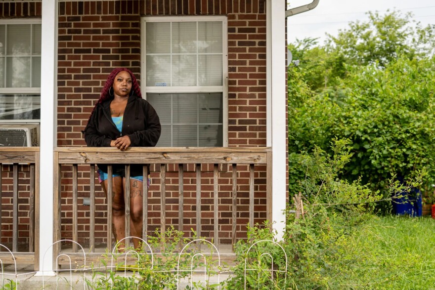 A woman poses on her front porch, in front of a brick red home.