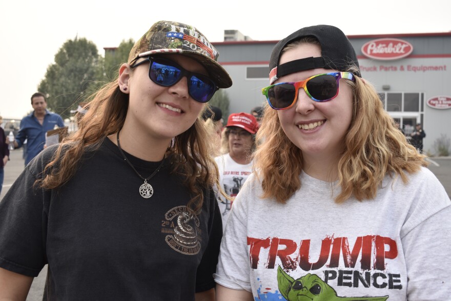 Two women, one is wearing a camouflage baseball cap that says, “Trump 2020,” and the other has a shirt that says, “Trump Pence,” with “Baby Yoda” on it. 