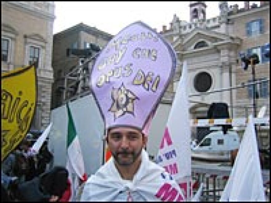 A demonstrator dons a paper bishop's miter with words "Better gay than Opus Dei."