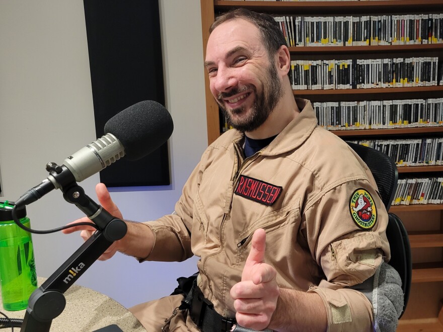 A man in a tan ghostbusters outfit sitting in front of a microphone