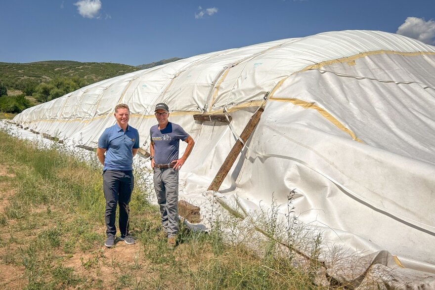Utah Olympic Legacy Foundation Chief Operating Officer Calum Clark (left) and Soldier Hollow Nordic Center Operations Manager Bill Pierce stand next to an artificial “glacier” of last season’s snow wrapped in an insulating blanket, July 30, 2026. A proof-of-concept project this year, the goal is to see if preserving snow over the summer to lengthen the winter ski season is feasible in a place like Utah.