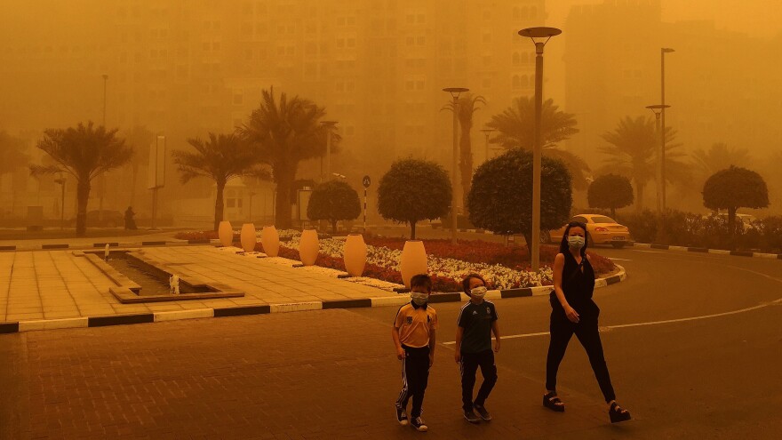 A woman and two children wear medical masks as they cross a street amid a sandstorm in Dubai.