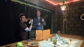 Colton Hughes and Wyatt Russ posing with foam weapons in front of a tabletop role-playing game map in a room designed to look like a castle