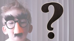 A child wearing Groucho Marx glasses; a question mark to the side