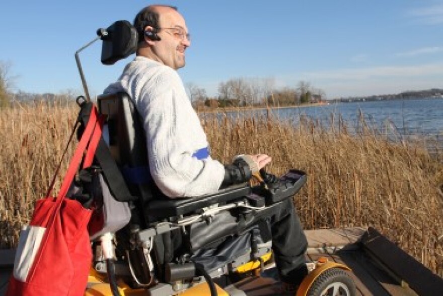 Dan Hawkins sits in a wheelchair beside a lake 