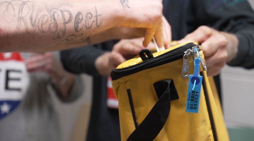 A person's forearm is shown, with a tattoo reading "Respect" as they vote by placing their ballot into a yellow bag, inside the Jefferson County jail on Nov. 5, 2024