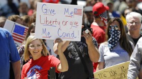 FILE - In this May 1, 2020, file photo, a protester holds a sign during an "Indiana Back to Work" rally at the Statehouse in Indianapolis. Indiana Gov. Eric Holcomb's statewide mask mandate and six months of other coronavirus restrictions has stirred discontent among conservatives, complicating his front-runner campaign against underfunded Democratic challenger Woody Myers.