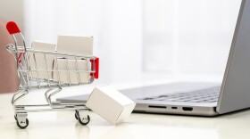 Tiny shopping cart with tiny packages on a table next to a laptop - Online Shopping Concept