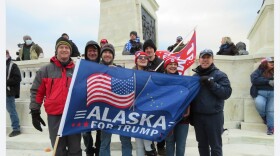 People stand on marble steps outdoors with flag that says "Alaska for Trump"