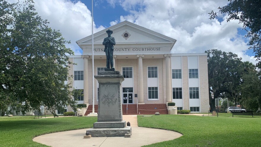 Confederate statue in the middle of the walkway outside the courthouse, large courthouse in the background.