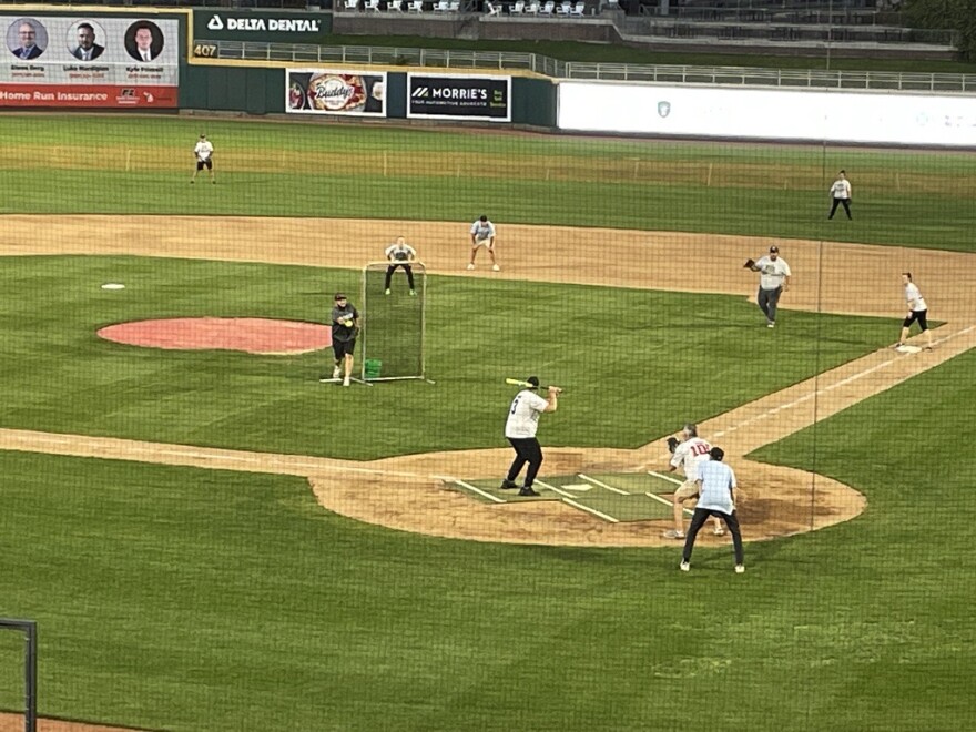 Rep. Alabas Farhat stands up to bat, with Rep. Tom Kunse as the catcher behind home plate.