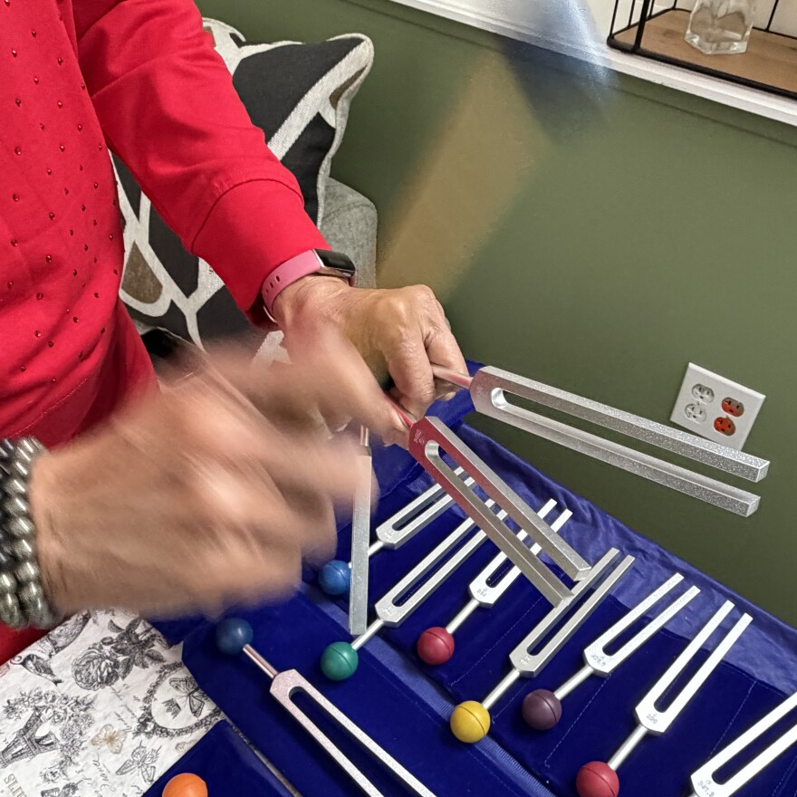 A closeup of Philana Crite's hands as she hits two tuning forks with a mallet.