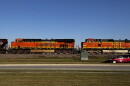 Two orange train cars with the BNSF and NSF logos ride along the train tracks on the side of a road.