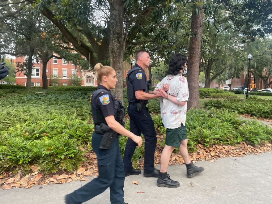 An unidentified University of Florida police officer holds the handcuffed hands of Allan Hektor Frasheri, 20, a philosophy major from Dunedin, Florida, after Frasheri's arrest late Monday, April 29, 2024, as campus police Officer Kristy Sasser walks behind them. Frasheri is facing a felony battery charge after Sasser accused him of spitting on her arm during the arrests of protesters on UF's campus. Frasheri, who is wearing a medical mask over his mouth in the photogaph, was being held in the Alachua County Jail on Tuesday, April 30, in lieu of a $5,000 bond.