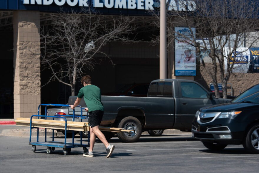 A customer wheels a cart of lumber across the parking lot at Lowe’s in Norman on May 8.