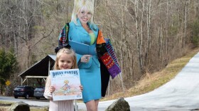 Girl holds a copy of Dolly Parton's book in front of a cardboard cut-out of the country singer.