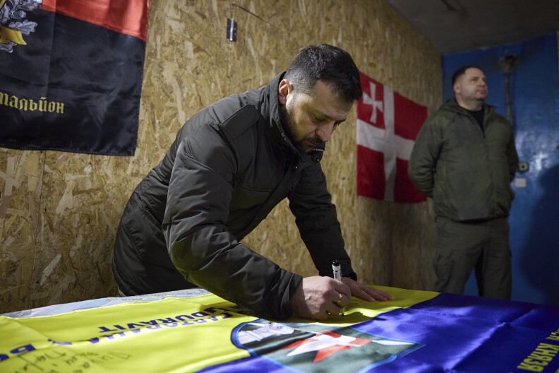 Ukrainian President Volodymyr Zelenskyy signs a flag during his visit to the front line city of Kupiansk, Kharkiv region, Ukraine, Monday, Feb. 19, 2024.