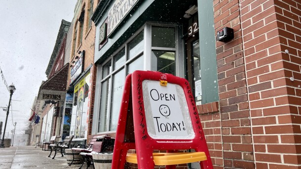 A sign on a child-sized easel reads, "Open Today!" It sits on a sidewalk outside a row of shops in Newton Falls.
