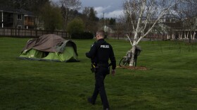 A police officer walks towards a green and brown tent in a camped-out field.