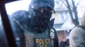 A masked U.S. Immigration and Customs Enforcement agent knocks on a car window in Minnesota on Jan. 12, 2026.