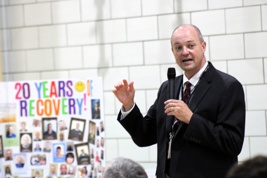 A man in a suit stands holding a microphone and giving a speech