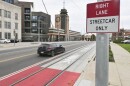 A city street is shown in the background with a single, black car driving one lane. In the lane nearest the camera, a red rectangle can be seen painted on the pavement where streetcar tracks are laid. A red and white sign in the foreground reads "Right Lane, Streetcar Only."