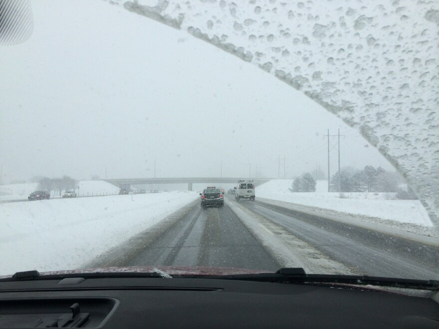 A picture of a snowy roadway through a windshield.