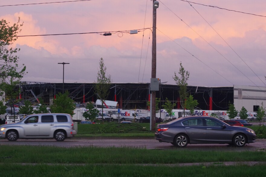 The FedEx building in Portage sits across the road. The side of the large white building has been ripped off by a tornado, with red beams and the dark interior of the building clearly visible. 