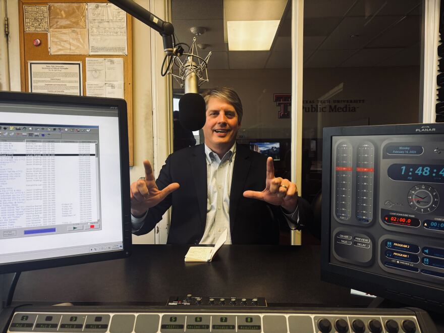 A photo of Tom Sell in the KTTZ studio. He is smiling and doing the Texas Tech 'guns up' hand sign.