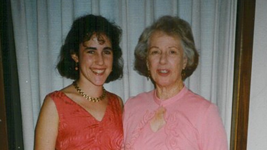 Two women, the younger to the left and older to the right, stand smiling next to each other.