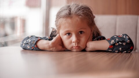 a sad little girl sits at a table with no food