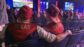 The backs of people wearing clothing that says "Texas" sitting in a conference room