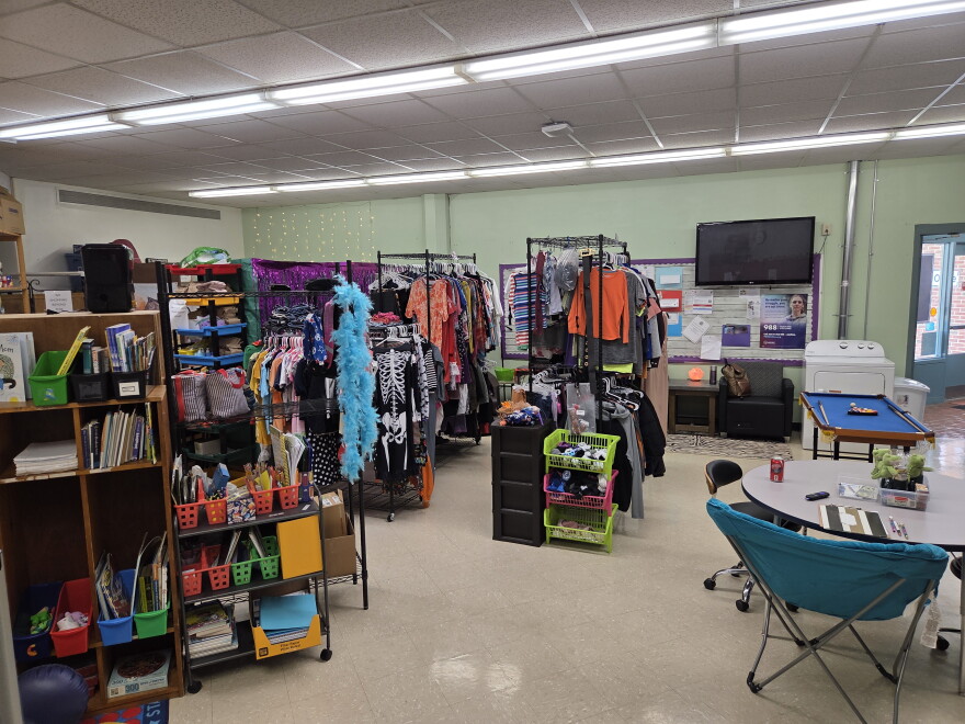 Racks of clothes, bookshelves, table and chairs in room