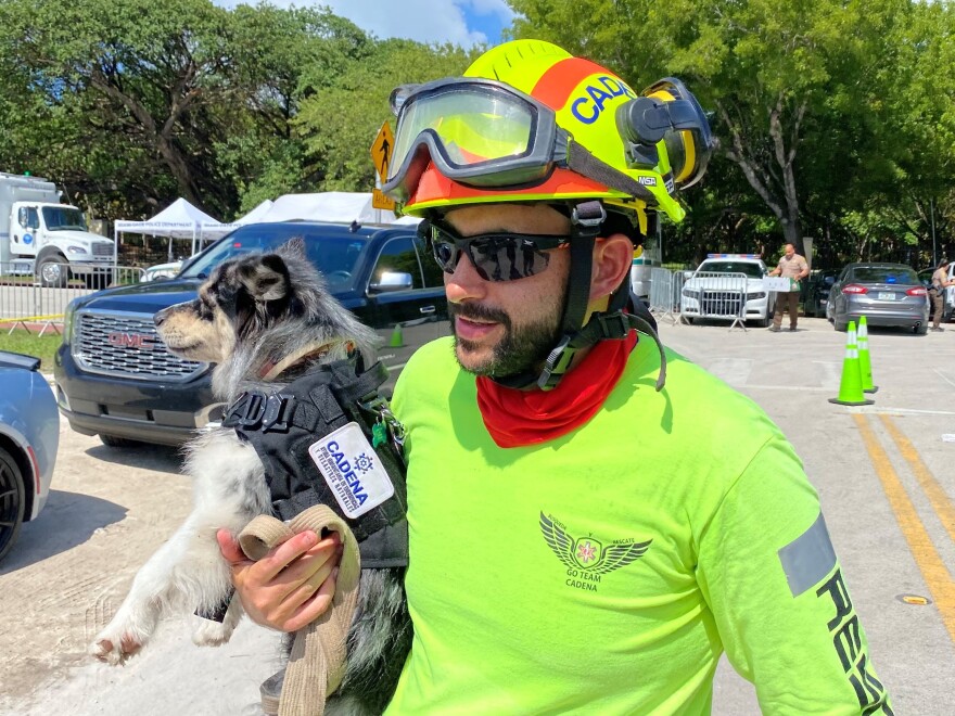 Moises Soffer, a volunteer member of Cadena International's search-and-rescue team working at the site of the condo building collapse, holds a trained search dog named Oreo in Surfside, Fla., on Sunday.