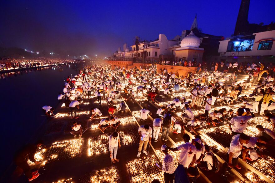 People stand over earthen lamps on the ground, which illuminate the banks of a river stretching as far as the eye can see.