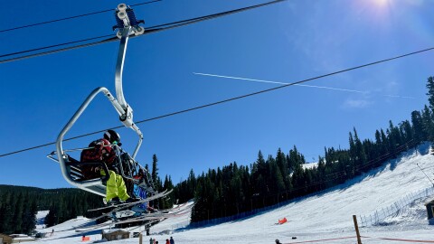 Skiers on a chairlift at Eldora Mountain on a sunny day