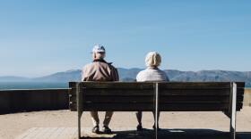 Man and woman sit on a bench facing the sea