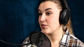 A woman wearing headphones and speaking into a recording studio-style microphone