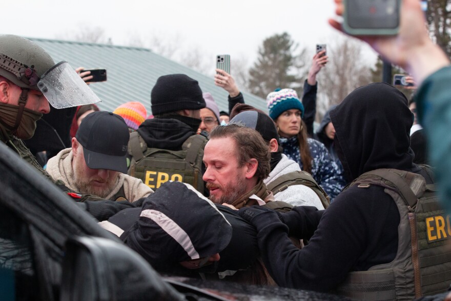 A man in a rain jacket is arrested on the hood of a law enforcement vehicle.